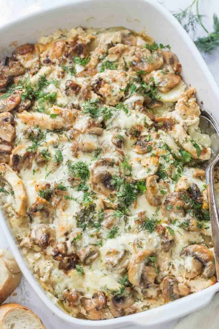Potato chicken mushroom casserole in a casserole dish with a spoon topped with fresh chopped dill.
