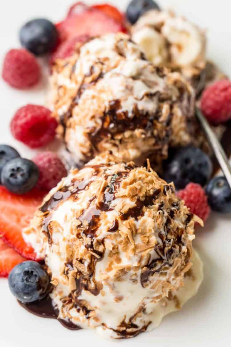 Vanilla ice cream balls in toasted coconut flakes on a plate with fresh berries. 