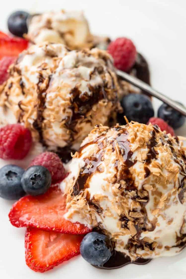 Two ice cream balls with berries on a white plate drizzled with chocolate. 