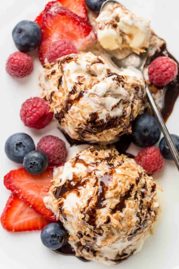 Two ice cream balls with berries on a plate topped with chocolate drizzle.
