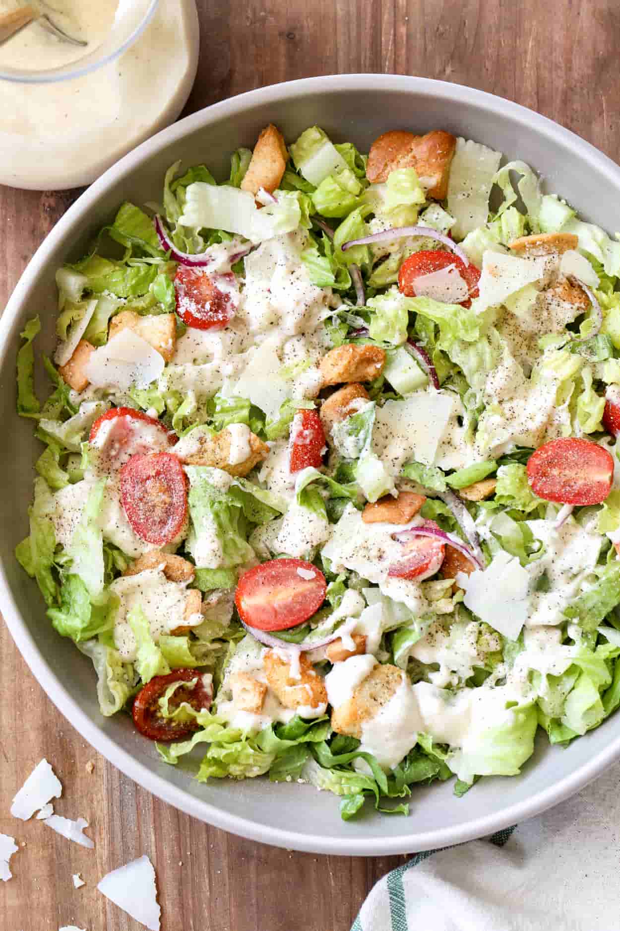 A bowl of salad with the Caesar salad dressing drizzled on top of the salad.