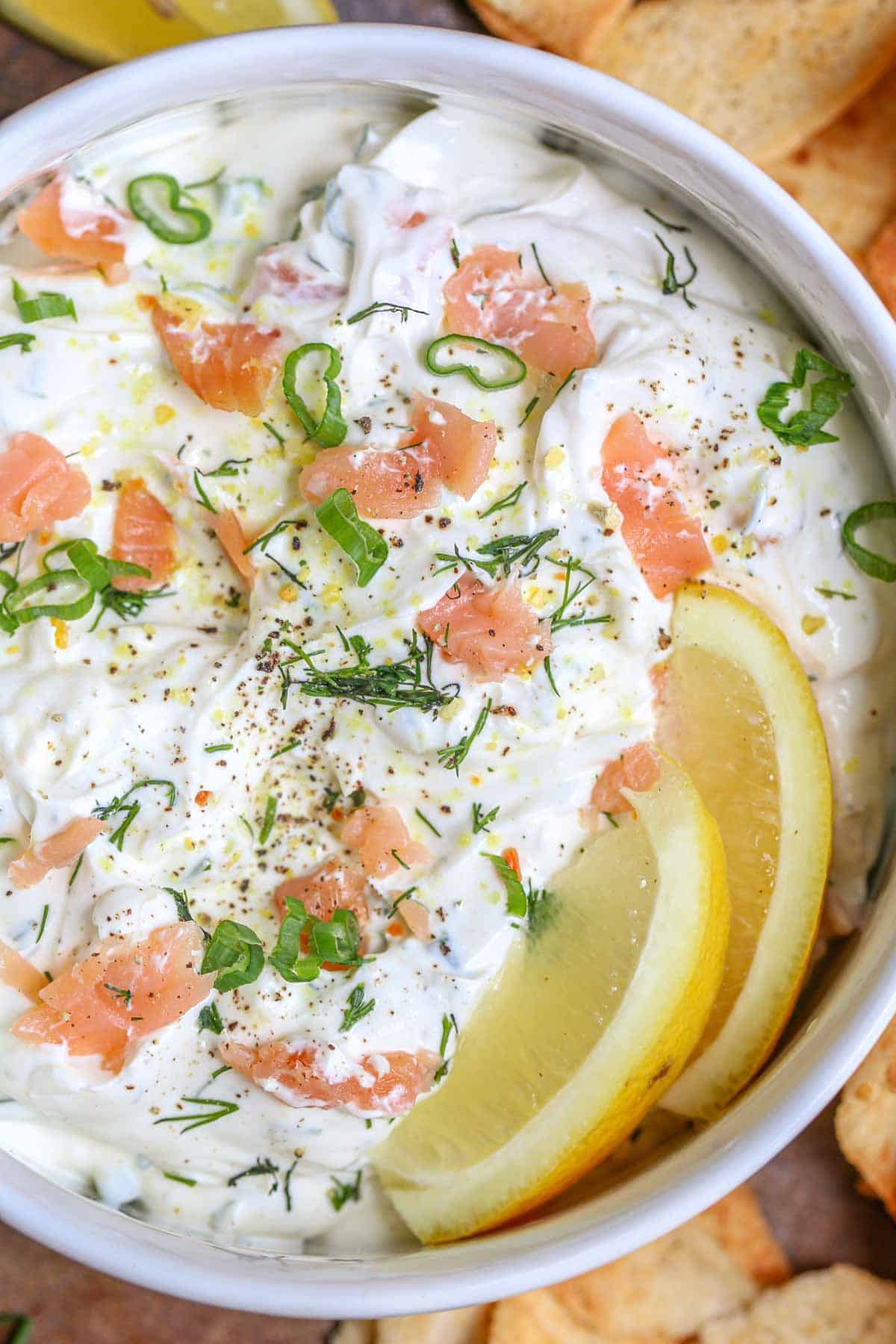 Cold smoked salmon dip in a bowl with lemon wedges and topped with greens. 