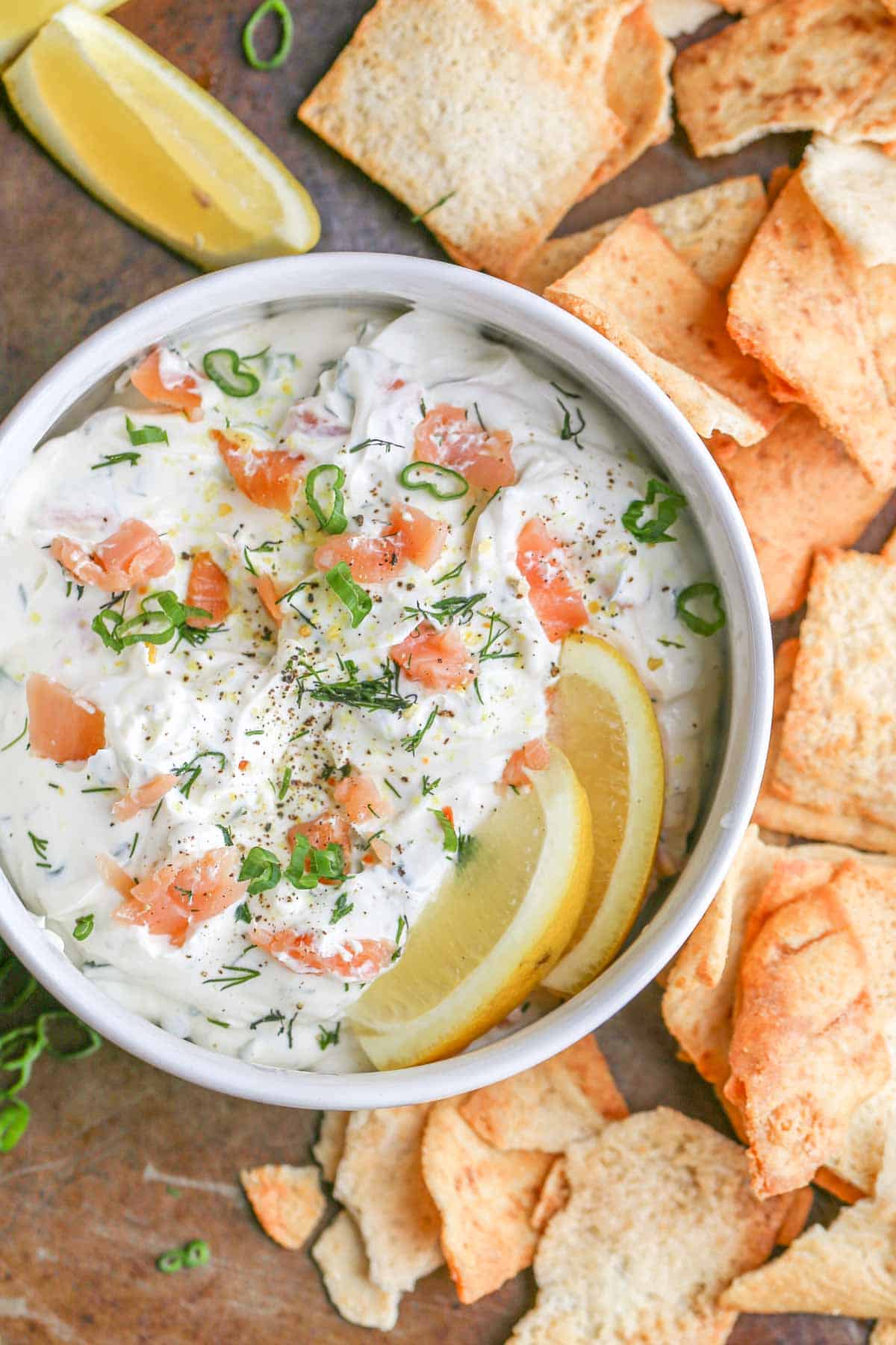 Dip topped with salmon and greens in a bowl with pita chips.