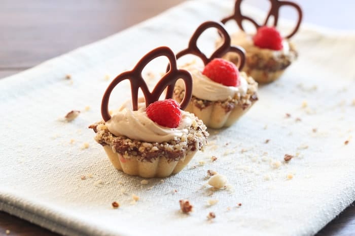 Mini tarts filled with chocolate and crushed walnuts and a dulce de leche cream on a platter.