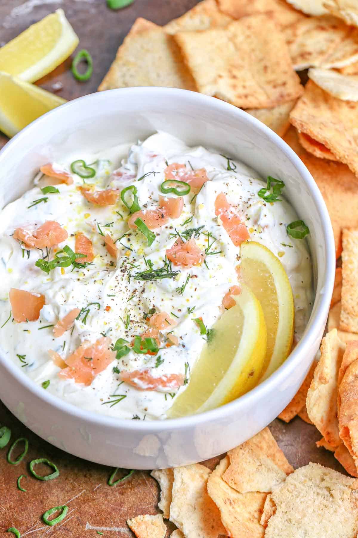 Cream smoked salmon dip in a white bowl topped with green onion and salmon pieces. 