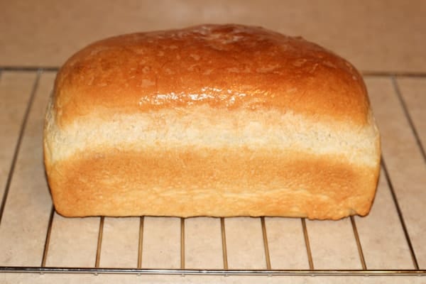 Homemade bread loaf on a cooling rack topped with butter.