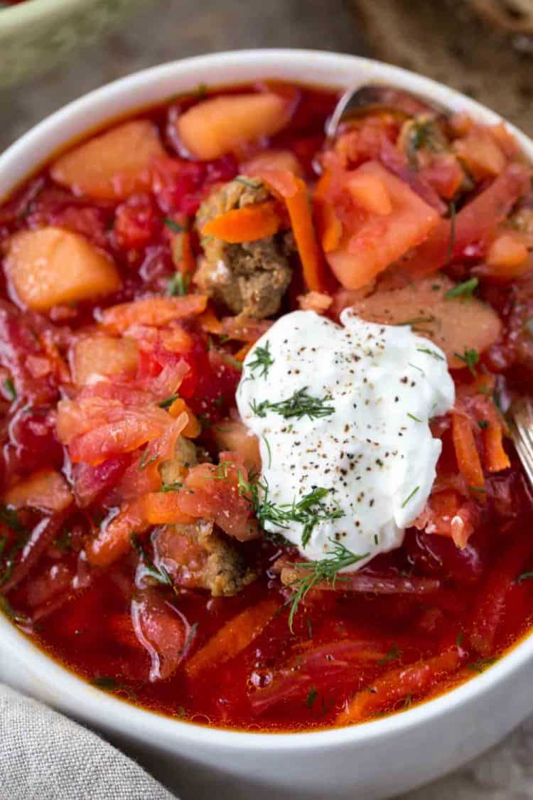 An up-close picture of Russian borscht in a bowl with sour cream, grated pepper, and fresh herbs.