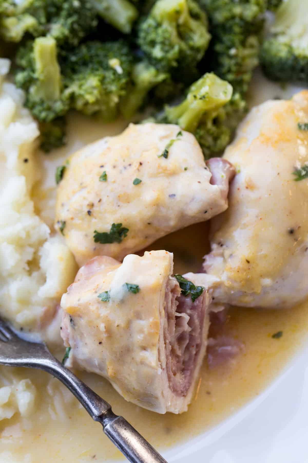 Chicken cordon bleu on a plate with a side of mashed potatoes and broccoli. Chicken rolled with ham and cheese.