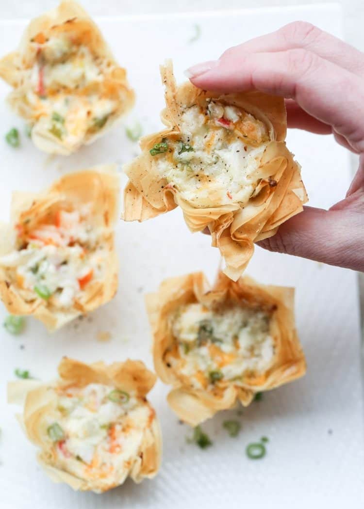 Seafood Phyllo Cups Appetizers with one being held topped with fresh greens.