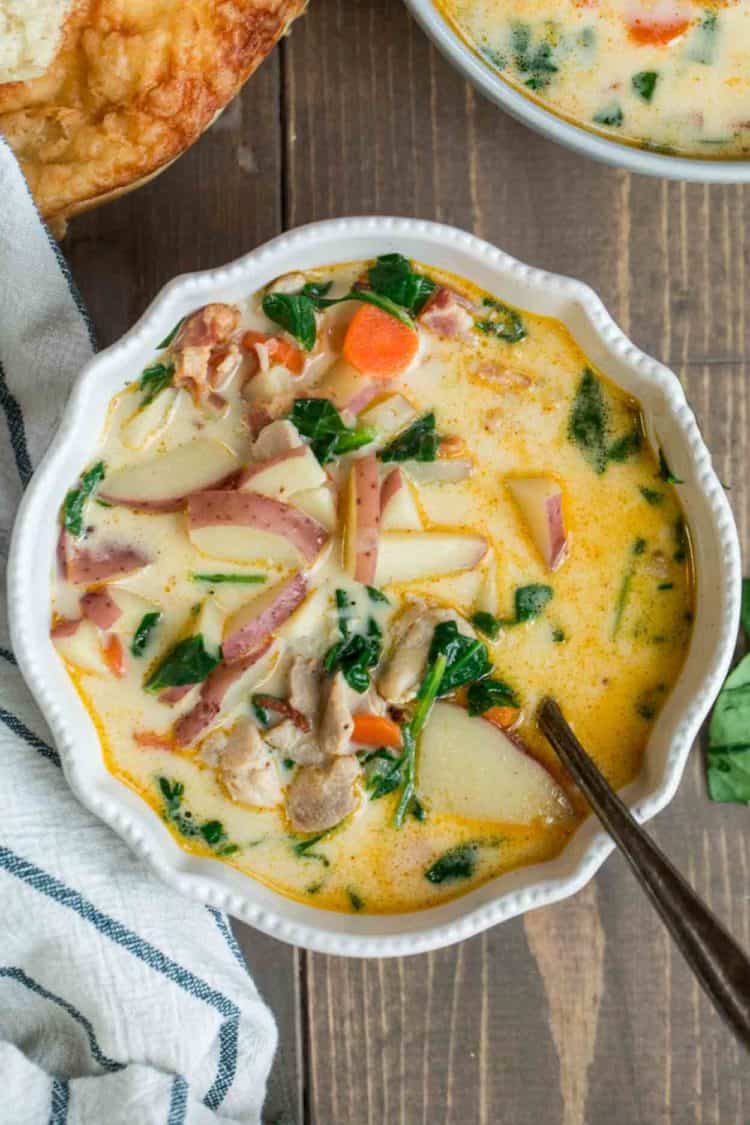 Creamy potato soup with chicken and spinach in a bowl with a spoon, next to bread and another bowl.
