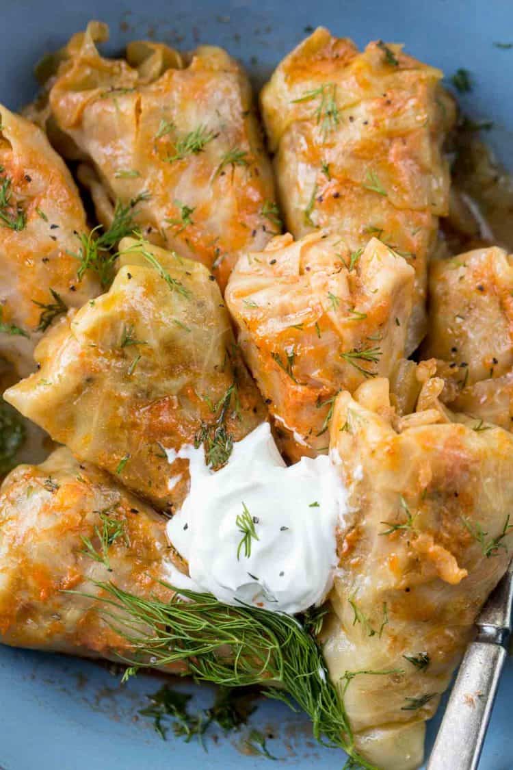 Stuffed cabbage rolls stacked on a place topped with sour cream and dill.