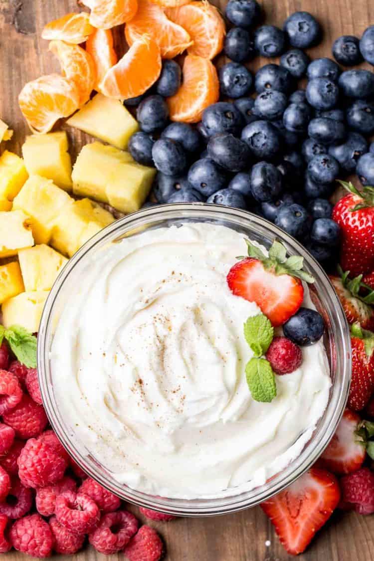 Cream cheese fruit dip in a bowl, next to raspberries, blueberries, strawberries and pineapple. 