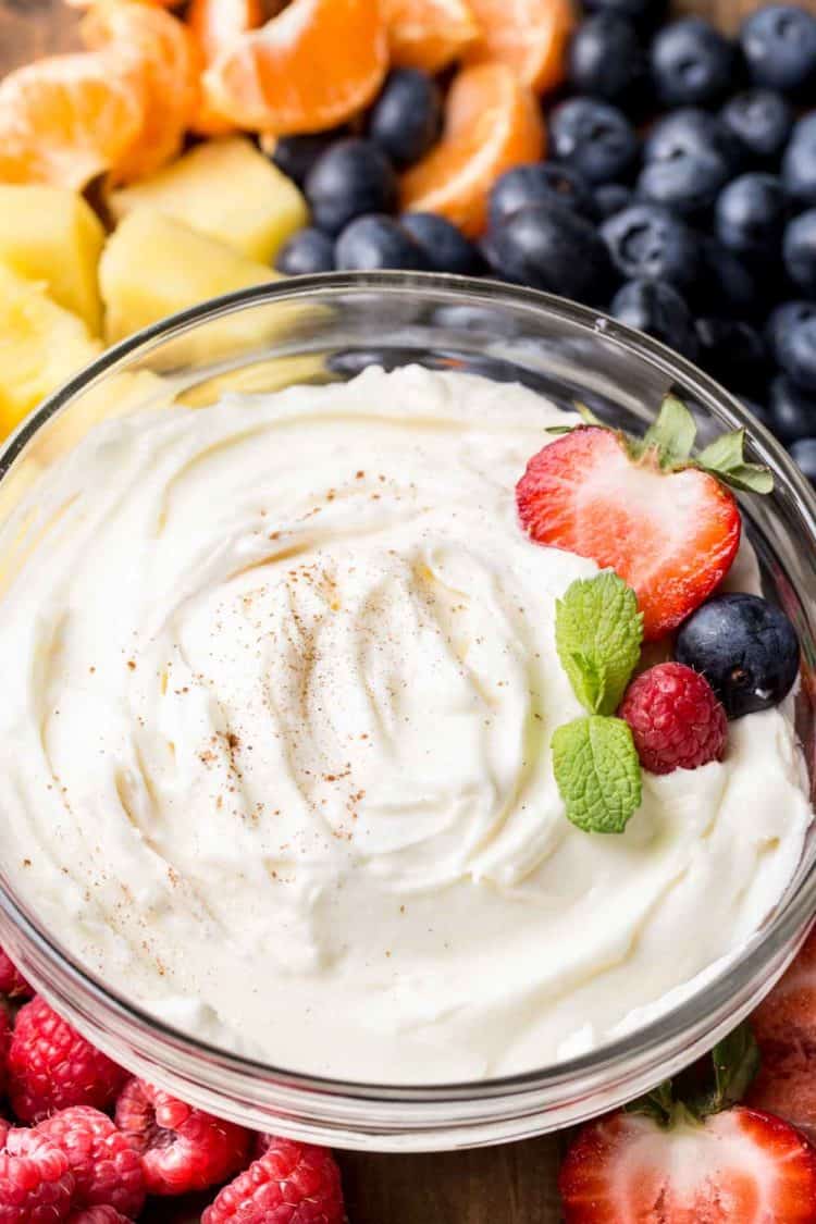 A glass bowl with cream cheese fruit dip next to fresh fruit. 