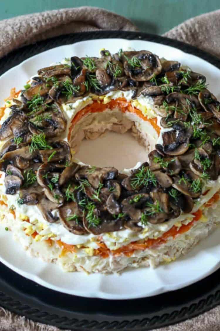 Layered chicken salad recipe on a platter topped with fresh greens. 