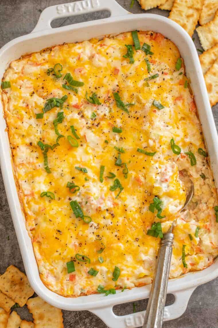 A white casserole dish with crab dip topped with fresh chopped greens.