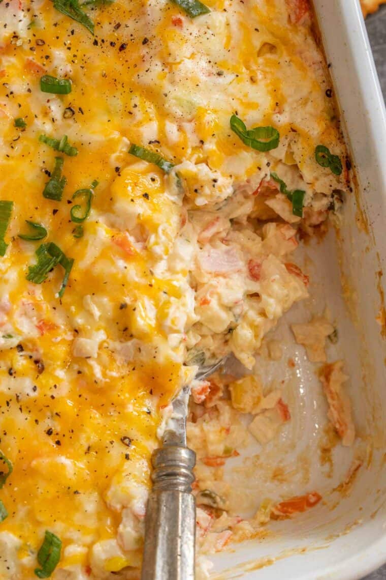 White casserole dish loaded with creamy hot crab dip topped with fresh chopped greens. 
