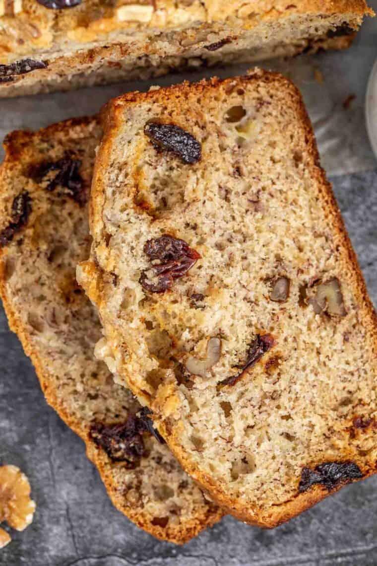 Slices of soft banana bread loaded with walnuts and dried fruit stacked on top of each other. 