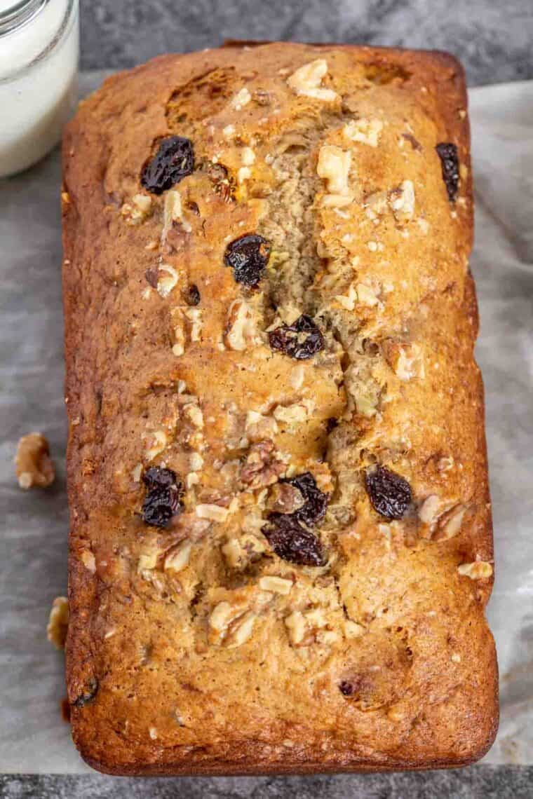 A loaf of banana bread on parchment paper topped with walnuts and raisins. 
