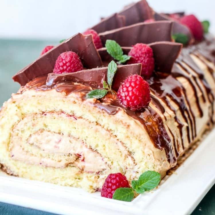 Cake roulade with a raspberry puree topped with chocolate drizzle and fresh raspberries. 