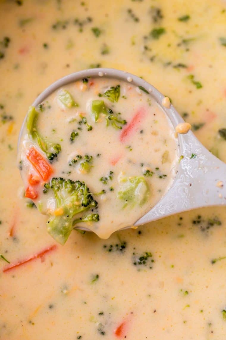 A ladle full of creamy broccoli cheddar soup loaded with cheese, broccoli and carrots.