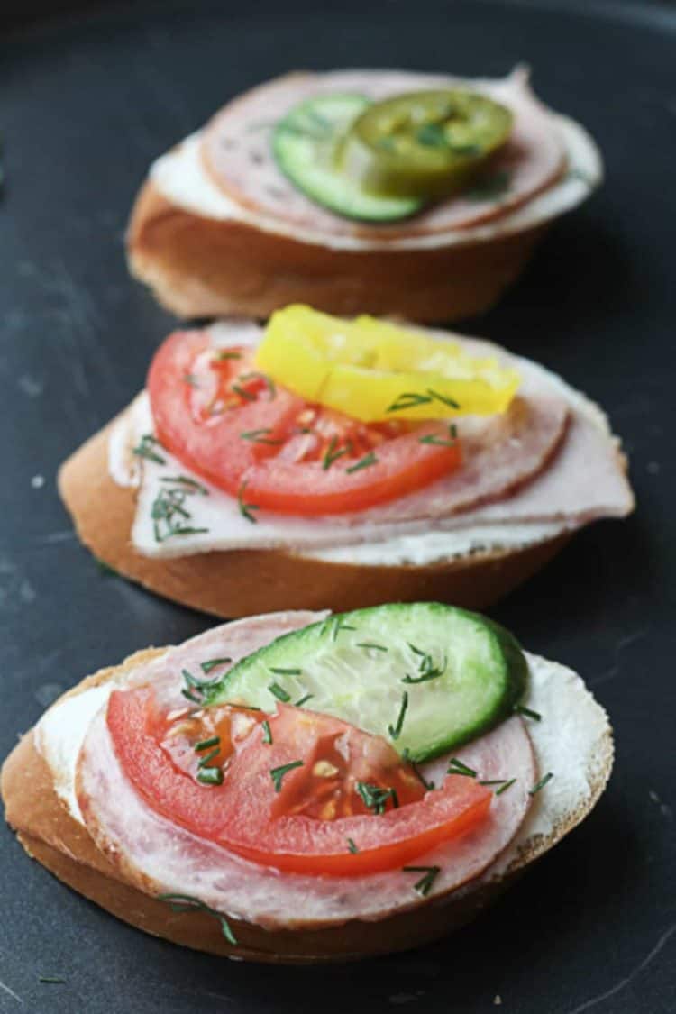 Canapes with a creamy spread topped with meat, tomatoes and cucumbers.