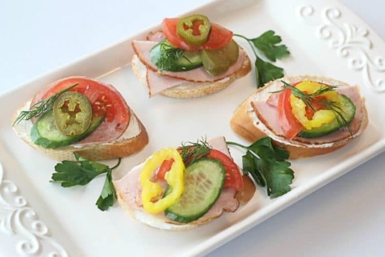 Canapes with a creamy spread on a tray topped with fresh greens