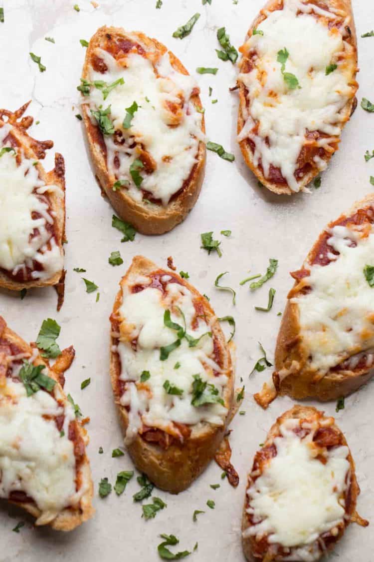  Cheesy pizza bite topped with fresh herbs, on a tray. Baguette topped with marinara sauce, pepperoni, and cheese!