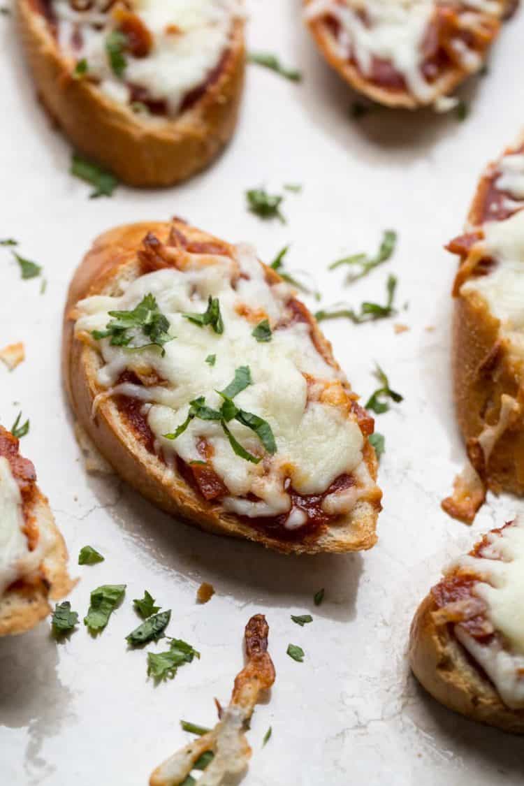 Bread slices with marinara sauce, pepperoni pieces, and cheese. Topped with fresh herbs.