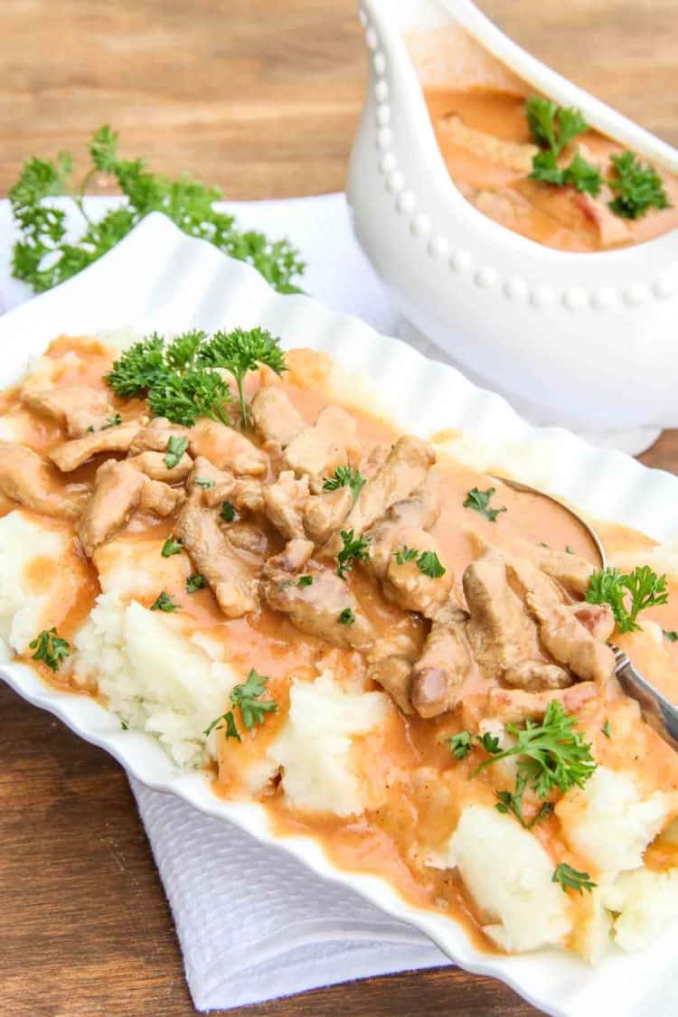 A creamy meaty gravy on a bowl with mashed potatoes topped with fresh greens.