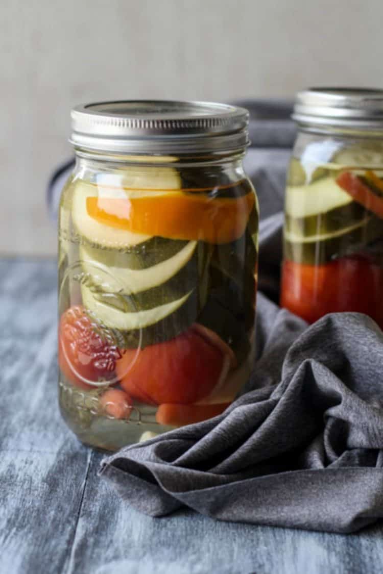 A mason jar filled with canned zucchini next to another jar and a gray rag.