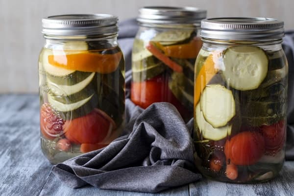 Three canning jars loaded with canned zucchini next to a gray rag.
