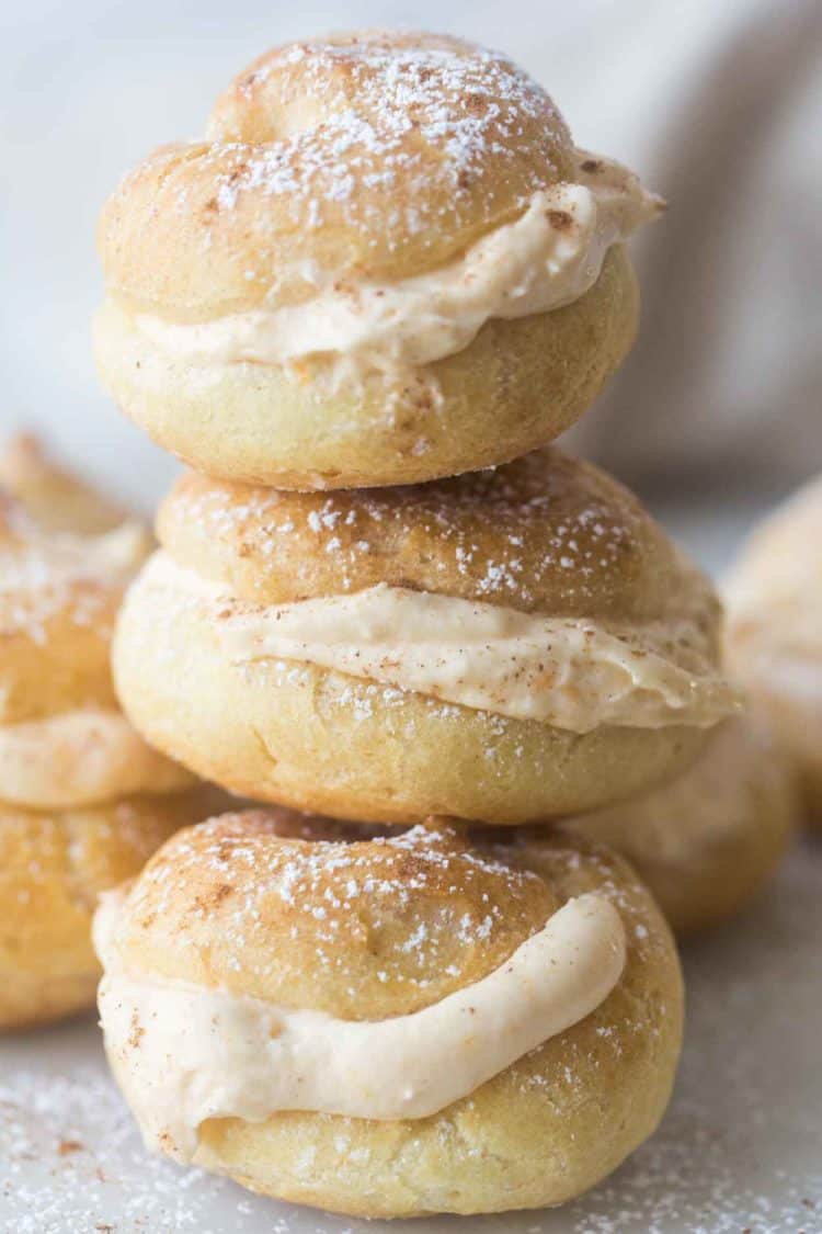 Pumpkin cream puffs stacked on top of each other topped with powdered sugar. 