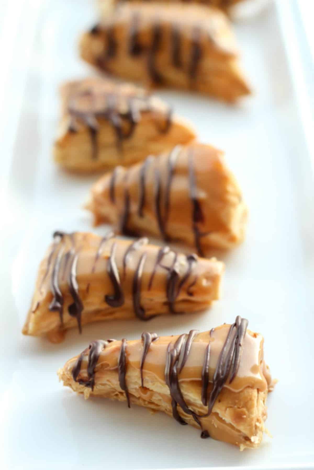 Puff pastry triangles with dulce de leche cream and chocolate drizzle on a platter.