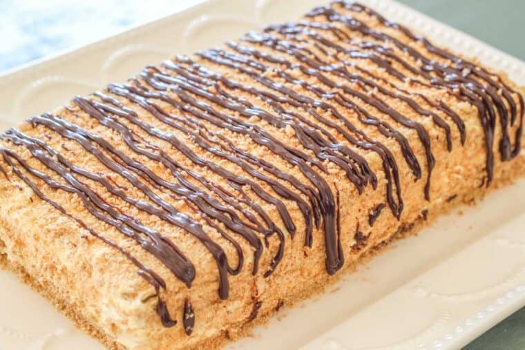 No bake éclair cake topped with chocolate drizzle on a white platter.