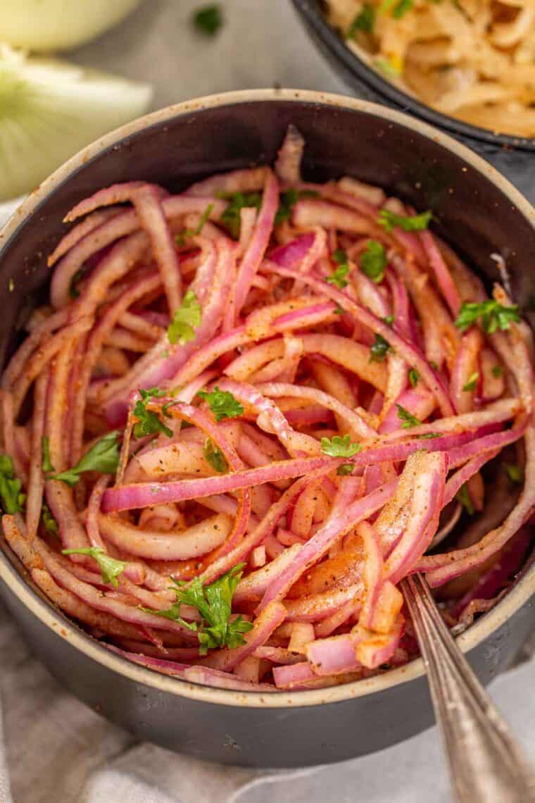 Red onion salad in a black bowl topped with fresh chopped greens and black pepper. 