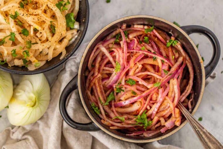 Two bowls of onion salad next to a rag and onion slices.