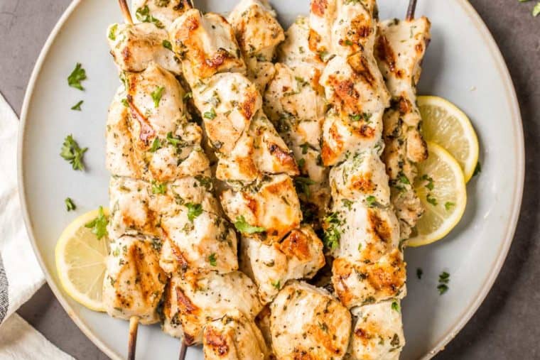 Grilled chicken kabobs on skewers topped with fresh greens next to lemons.