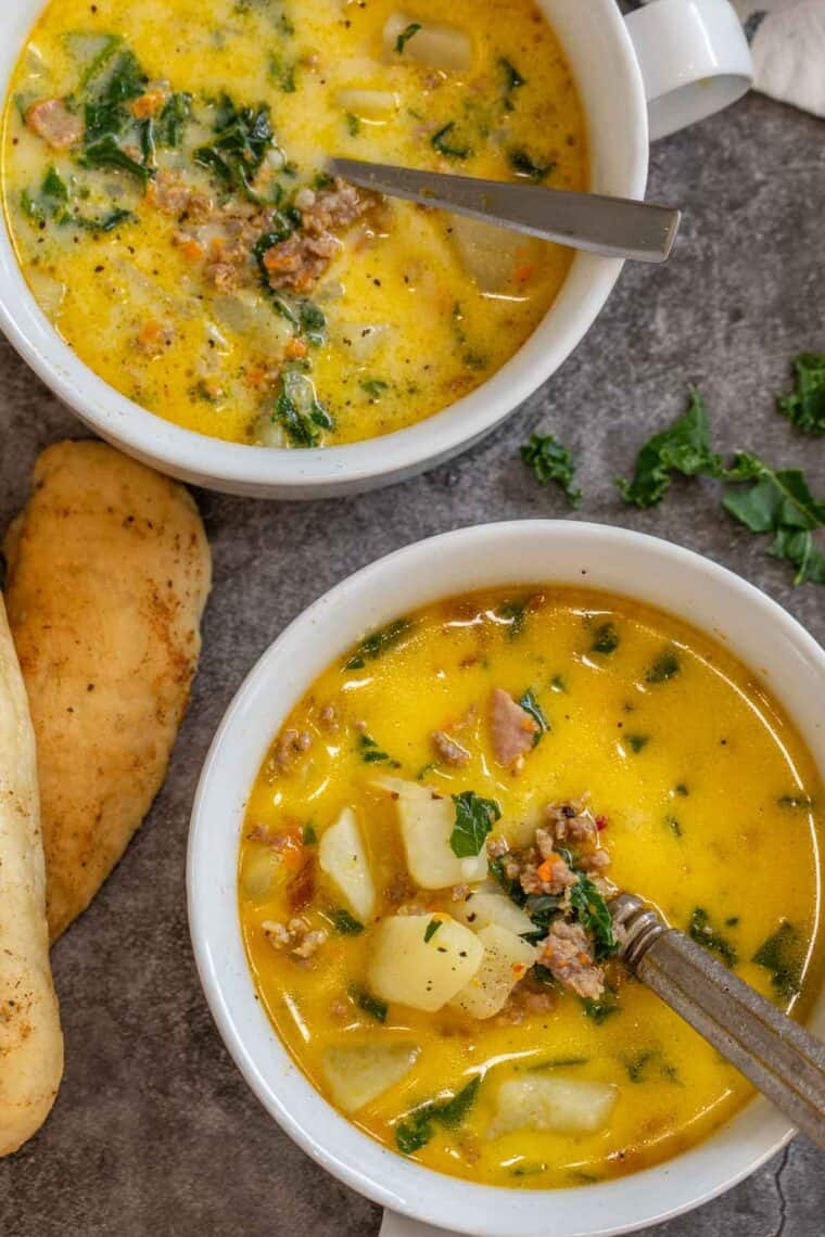 Two bowls of zuppa toscana soup next to homemade breadsticks. 
