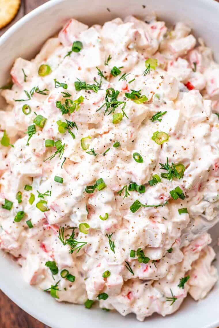 Cold crab dip in a white bowl with chopped greens. 
