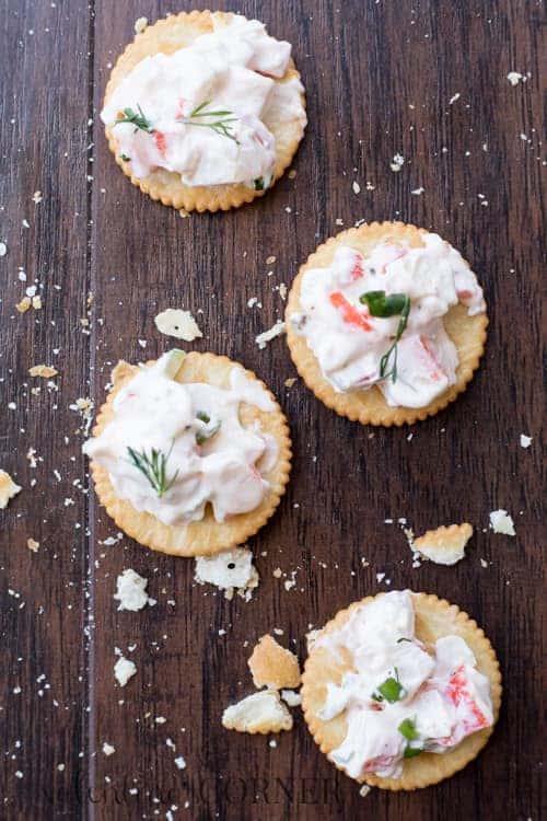 Four crackers with crab dip on them with crumbs all around.