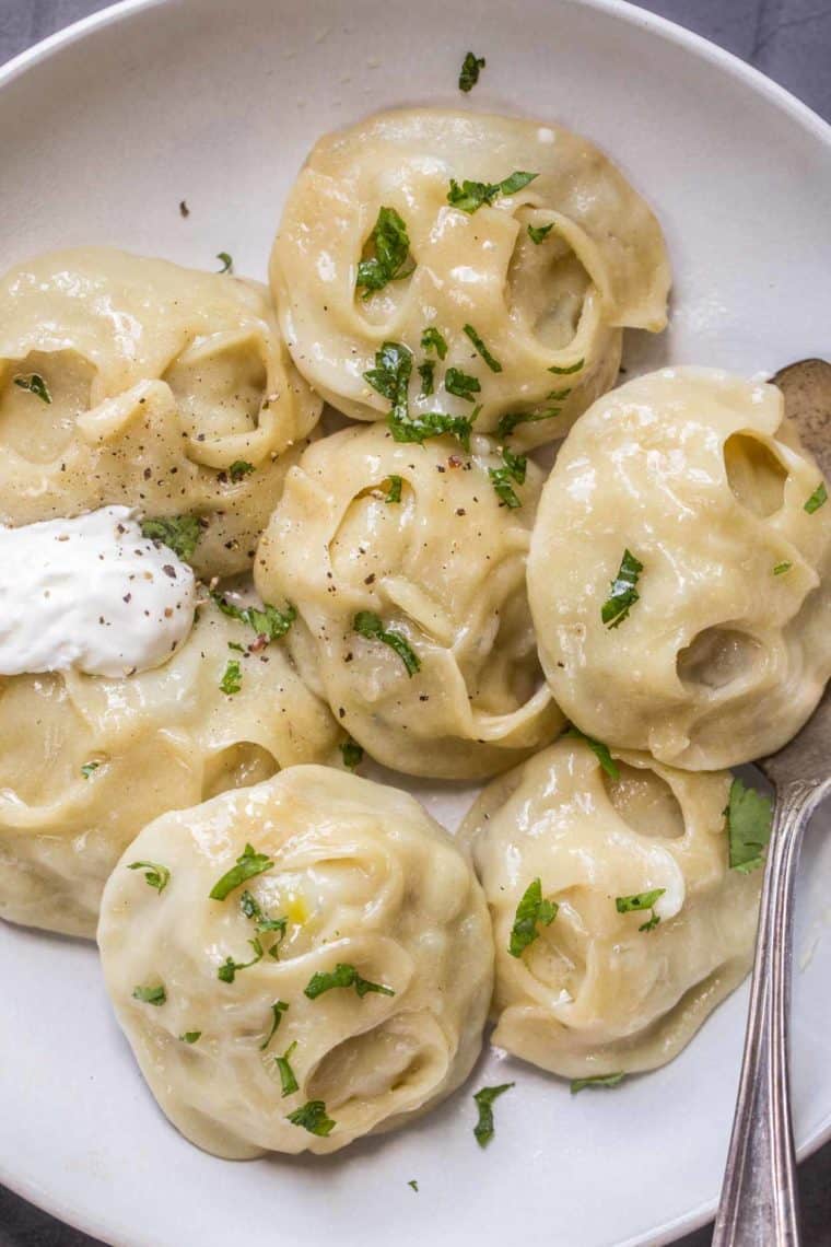 Steamed and buttered Uzbek Manti on a plate with a fork and sour cream.
