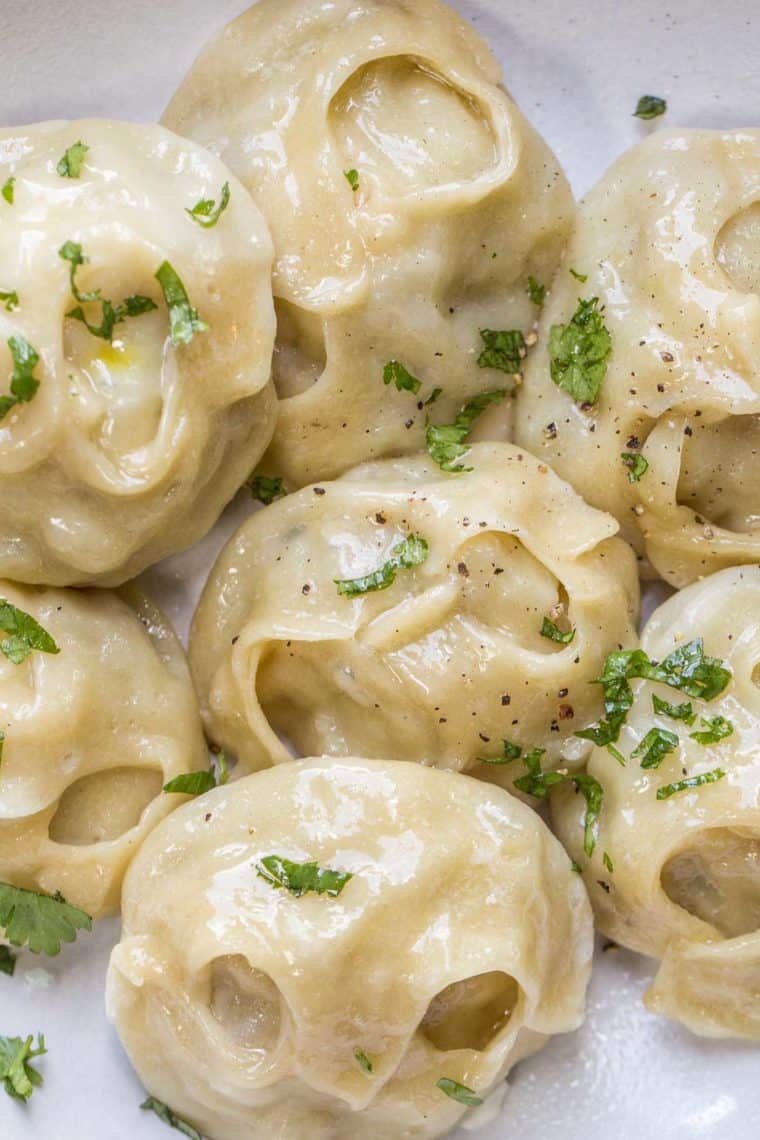 Manti dumplings in a white plate topped with fresh greens and ground black pepper.