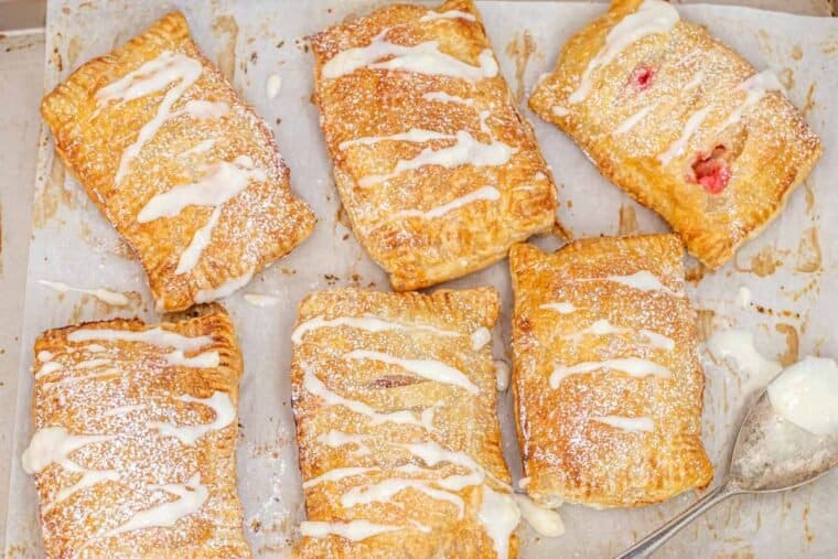 Puff pastry cherry hand pies drizzled in sweet glaze in a baking sheet. 