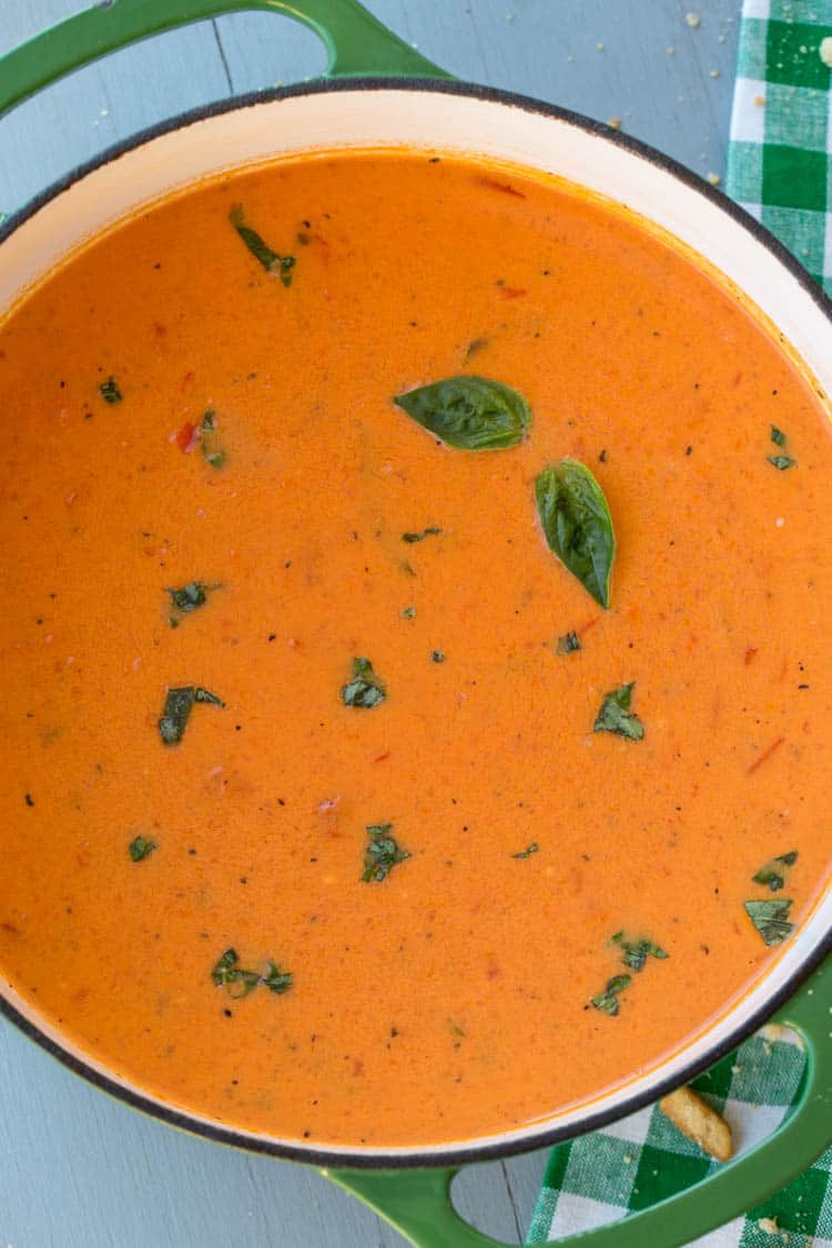 Creamy tomato soup with basil in a dutch oven topped with fresh basil. 