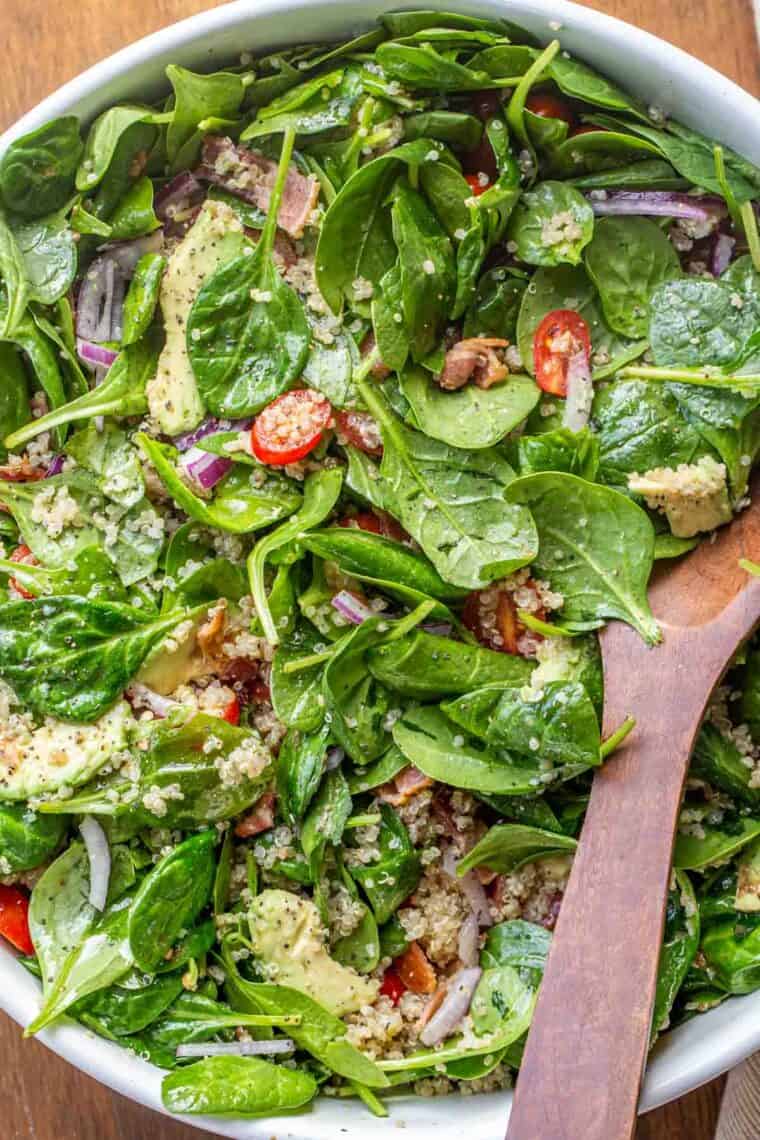 Spinach quinoa salad recipe tossed in dressing in a white salad bowl. 
