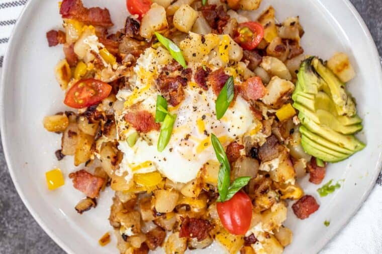 A white plate loaded with breakfast skillet potatoes, eggs and bacon. 