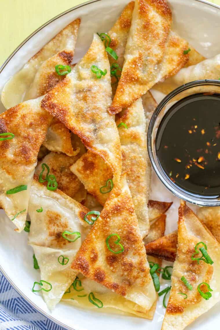 Pork potstickers in a plate topped with green onion next to a bowl of soy sauce. 