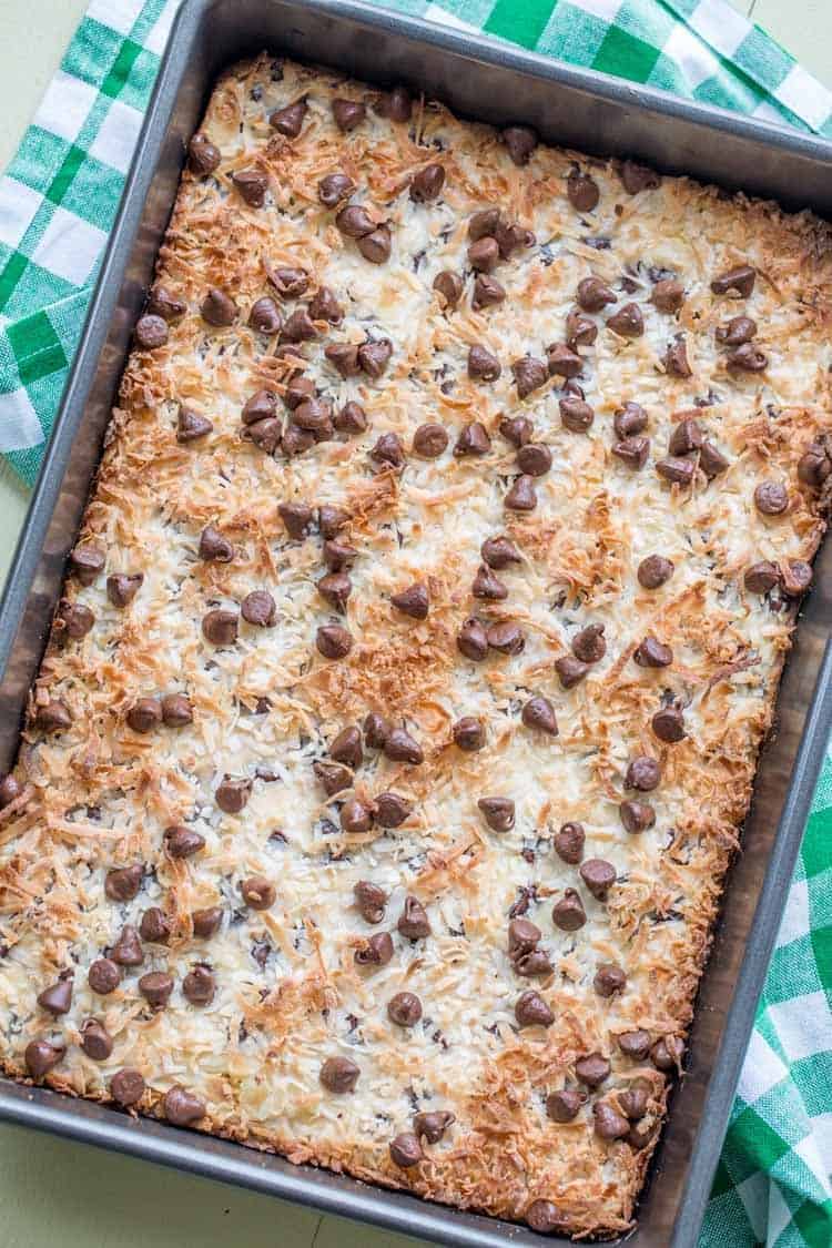 Cookie bars in a baking sheet topped with chocolate chip morsels and coconut shavings in a baking pan.