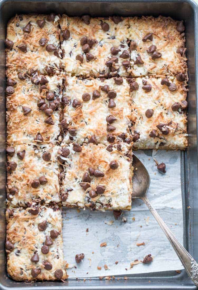Magic cookie bars recipe in a baking pan cut into pieces with a spoon.
