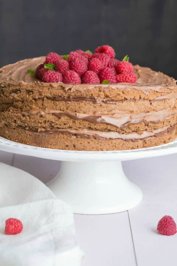 Homemade chocolate cake recipe Nutella cream and raspberries on a cake platter.